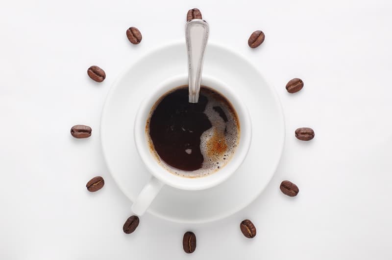 A mug of coffee with coffee beans spread around it