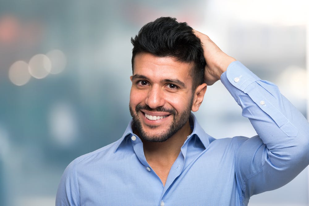 A man feeling the top of his head as he has a full head of hair following a hair transplant