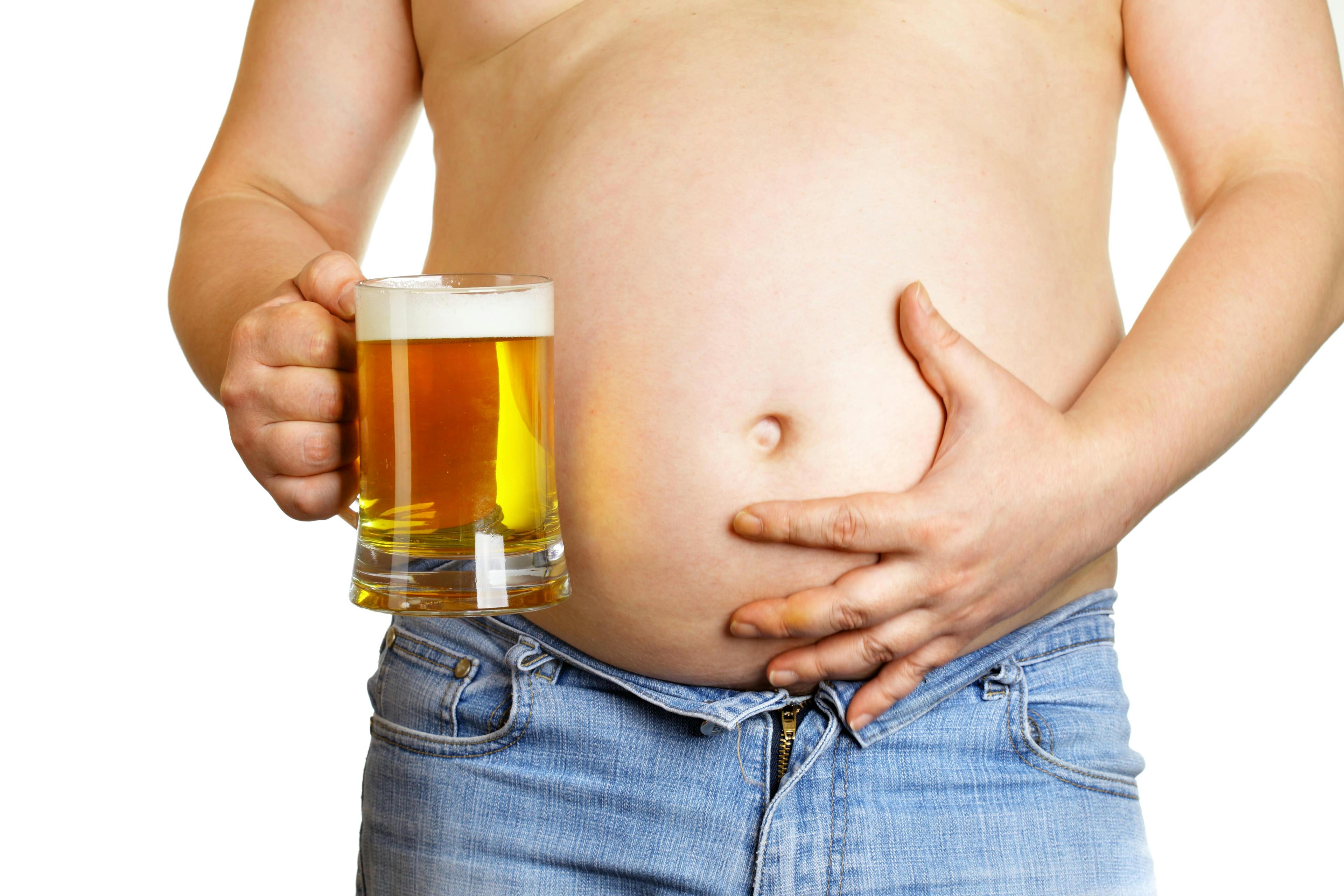 A man with a beer belly holding his stomach and a glass of beer